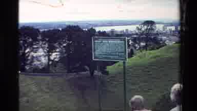 New Zealand (1981): A Hill With A Sign Going Down With A Green Grass And A Tree At