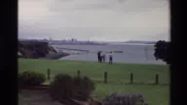 New Zealand (1981): Woman In Pink Dress Several People Walking Near Water Stone