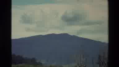 New Zealand (1981): Rocky Mountain Covered In Pine Trees With Large Dark Clouds