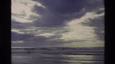 New Zealand (1982): Sun Peaks Through Thick Clouds Lining Sky Over Oceans Waves