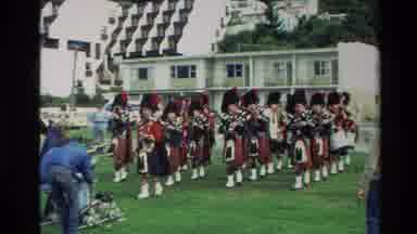 New Zealand (1982): Group Of Bagpipe Players Being Filmed Playing While Walking
