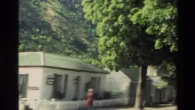 New Zealand (1982): Women In Red Dress Walking Down Street Of Homes Lined With