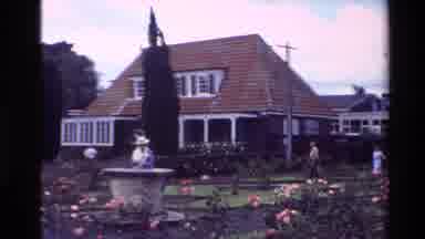 New Zealand (1981): People Walking Around A Garden And The House Behind It