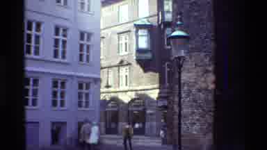 Denmark (1982): A Very Tall White And Brown Building As People Walk Across The