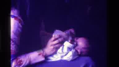 California USA (1975): Woman Holding Baby On Her Lap While Feeding Baby With