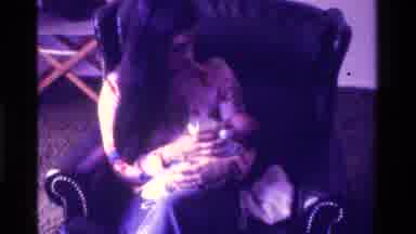California USA (1975): Woman Sitting In An Armchair Feeds Baby With Bottle