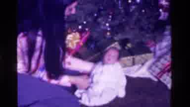 California USA (1975): Mother Holding Sleeping Baby Up In Front Of A Christmas