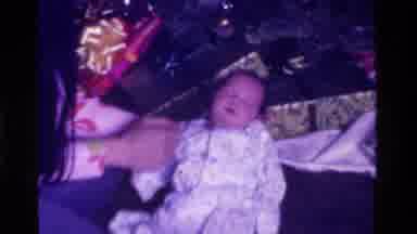 California USA (1975): Newborn Baby Being Held By A Christmas Tree Near Christmas