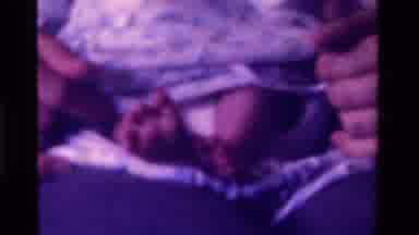 California USA (1975): Adult Hands Tickle Feet Of Newborn Baby Wearing Soft Sleep