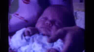 California USA (1975): Woman Holding Baby And Placing It Into A Crib