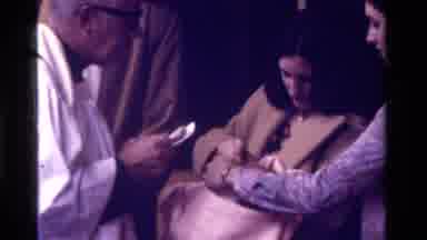 California USA (1975): Mother Surrounded By Family While Priest Baptizes Her