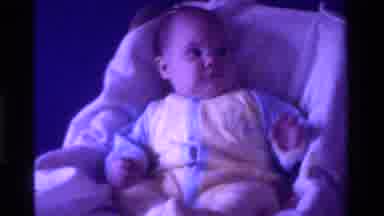 California USA (1975): Mommy Giving Baby A Rattle While Baby Is In A Car Seat