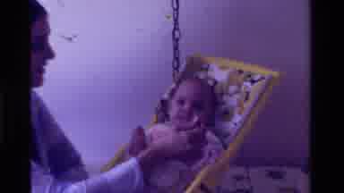 California USA (1975): A Father Feeding An Infant Some Baby Food In An Infant Seat