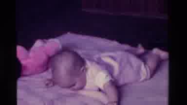 California USA (1975): Baby Lying On Its Belly And Rubbing Its Left Eye With A