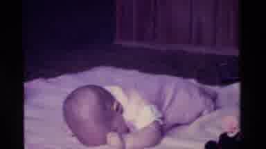 California USA (1975): Baby Playing On Bed With A Teddy Bear And Also Sucking