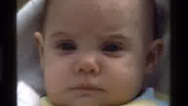 California USA (1975): Baby In A Blue And Yellow Top Blinking At The Camera