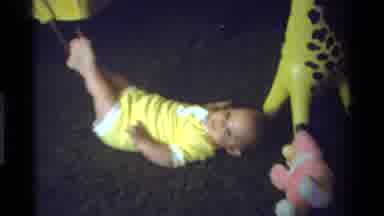 California USA (1975): Baby Dressed In Yellow Lying On The Ground While Rubbing