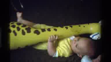 California USA (1975): Baby Playing With Blow Up Giraffe On The Floor Wearing