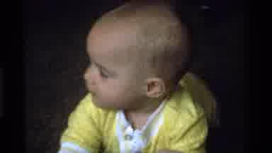 California USA (1975): Toddler In Yellow Onesie Lying On Carpeting And Playing