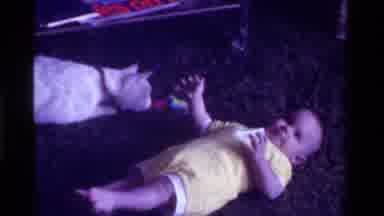 California USA (1975): White Cat Looks At Baby Wearing Yellow Onesie Lying On