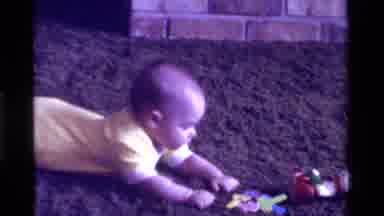 California USA (1975): Toddler In Yellow Onesie Lying On Stomach On Carpeting And