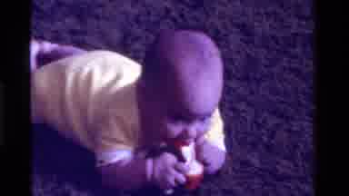 California USA (1975): Beautiful Baby In Yellow And White Clothes Is Chewing On A