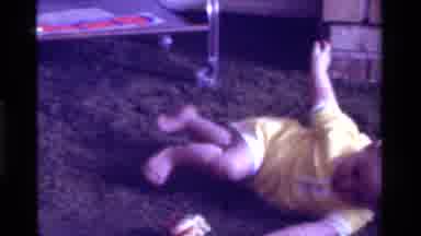 California USA (1975): Newborn Baby Playing On The Floor Next To His Mother