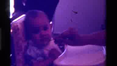California USA (1975): Feeding Baby With Spoon And Cleaning Its Face With A Cloth
