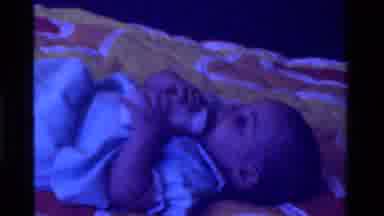 California USA (1975): An Infant Lies On A Blanket On The Floor And Kicks While