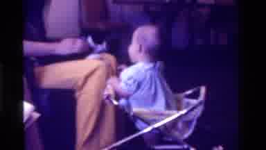 California USA (1975): Baby Wearing Blue Dress Sits In Walker Petting Black And
