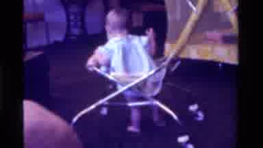 California USA (1975): Infant Learning How To Walk In Walker In Living Room Of