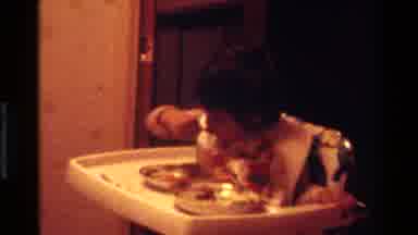 California USA (1977): Young Child Eating While Sitting In High Chair Wearing Bib