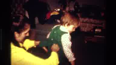 California USA (1977): A Mother Dresses Her Toddler Daughter In A Green Outfit