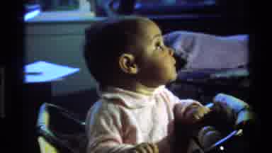 California USA (1977): Baby In A Walker Looking Up And Around At Something