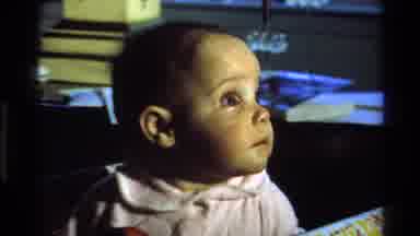 California USA (1977): Little Baby Dressed In White Staring At Something In The