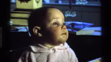 California USA (1977): Old Film Of Curious Brunette Baby Girl On Walker Indoors