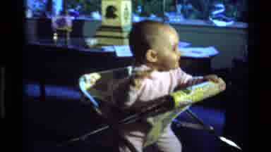 California USA (1977): A Baby In A Pink Onesie Bounces Up And Down In A Chair