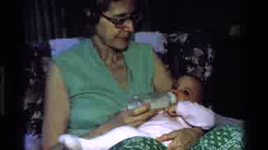 California USA (1977): Infant Being Fed With Glass Bottle By A Caring Green Shirt