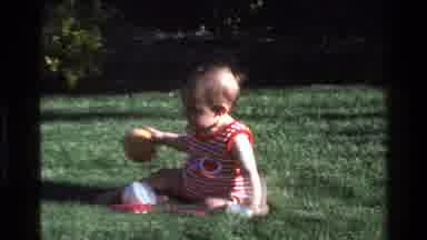 California USA (1977): Toddler In Striped Onesie Sitting And Crawling On Grass And
