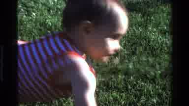 California USA (1977): Baby Crawling On Grass In Striped Onesie To Parent With A