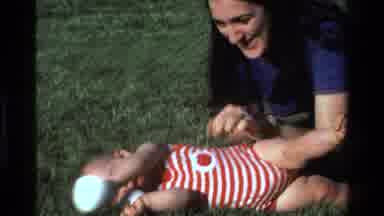 California USA (1977): Baby In Red Striped Onesite Holding Two Cups And Being