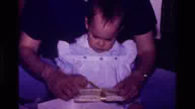 California USA (1977): Baby Girl Unwrapping Gifts On Christmas Day In Mom's Lap