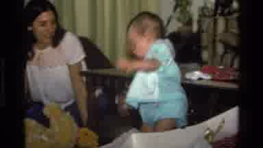 California USA (1977): A Baby In A Green Dress Dances And Examines A Blanket A