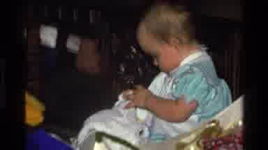 California USA (1977): A Baby In A Green Dress Playing With A Toy In The Living