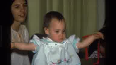 California USA (1977): The Baby Girl Turns Around Carrying The Red String In Her