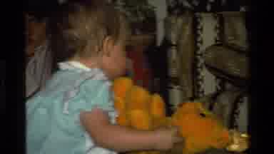 California USA (1977): Baby In Party Playing With A Ball And Orange Teddy Bear