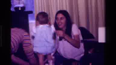 California USA (1977): Family Members Helping Young Child Open And Play With