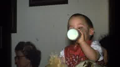 California USA (1977): Child Taking Porridge In The Bottle Dressed As A Bib With A