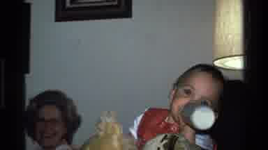 California USA (1977): Baby Wearing Red And White Shirt Drinks From White Baby