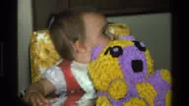 California USA (1977): A Baby Sitting Behind A Yellow Crochet Teddy Bear While
